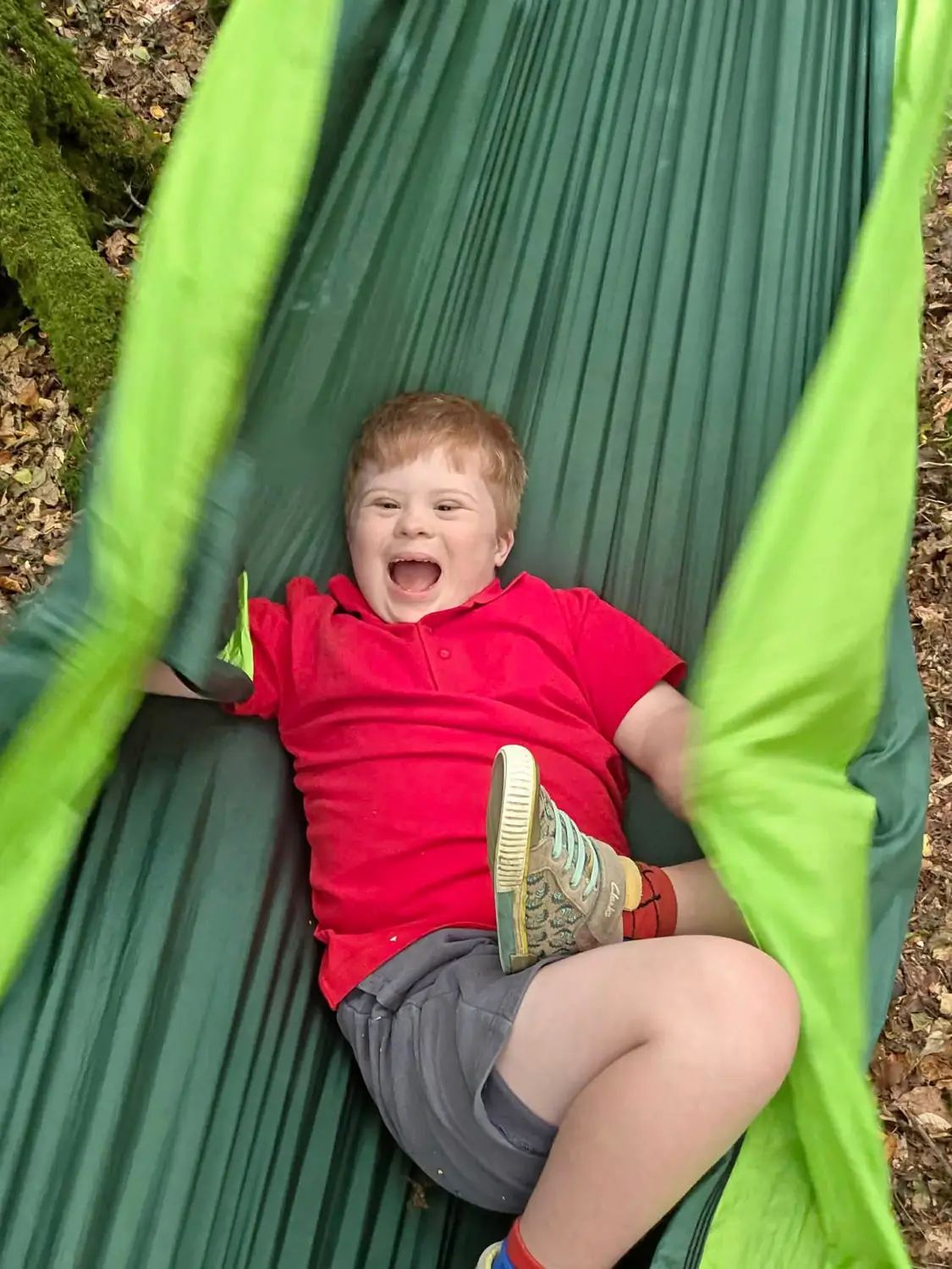 A child lying in the green hammock, laughing